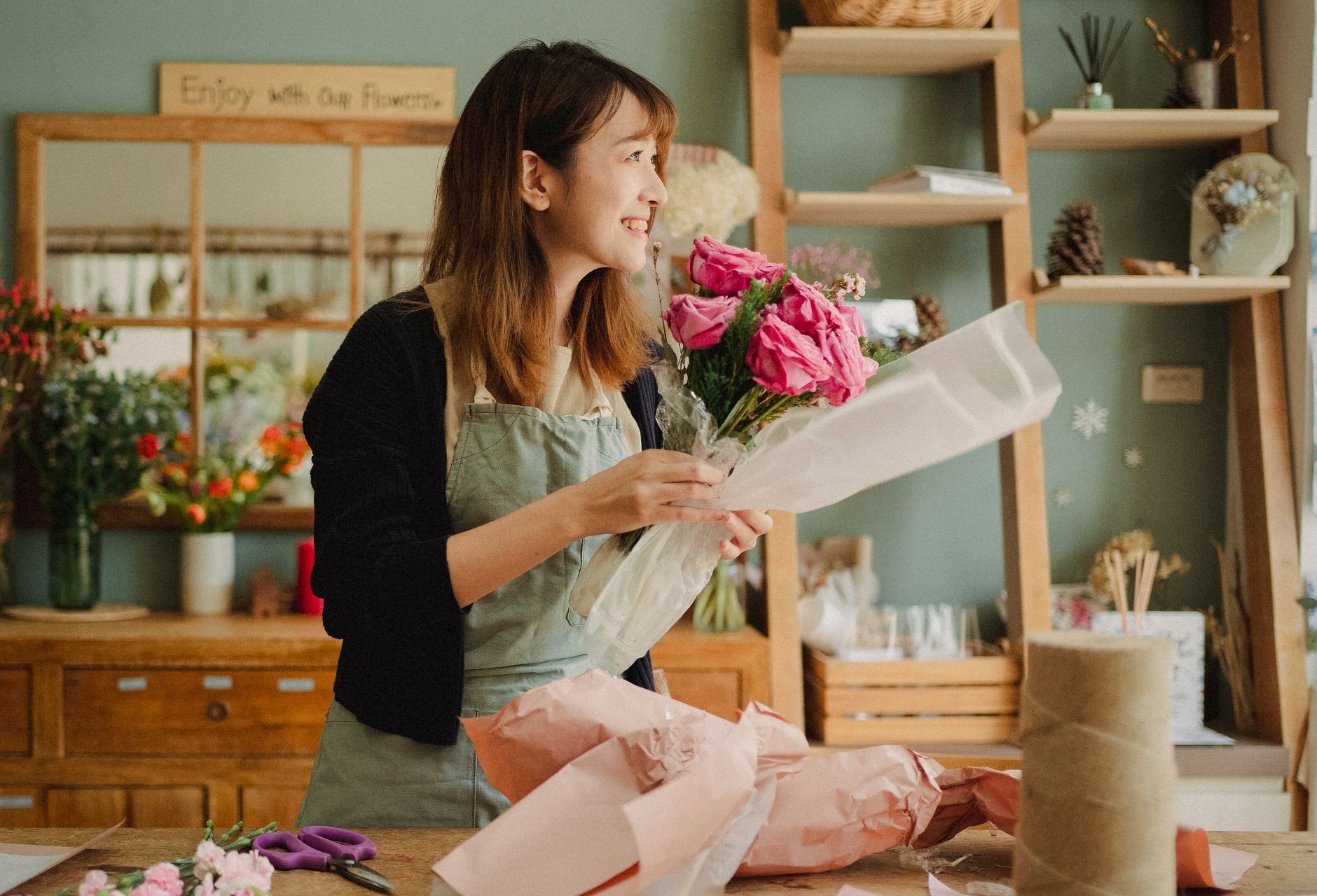 A florist in an apron tying a bouquet of roses at her workbench